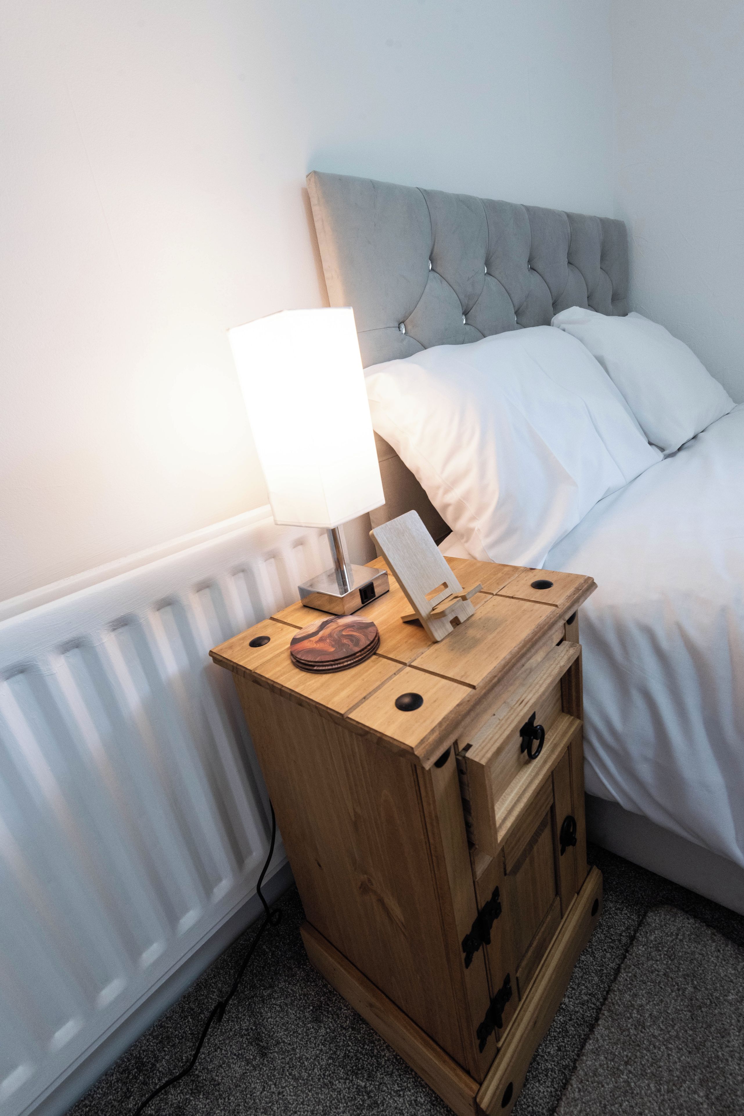 A wooden bedside table with a lamp, a small wooden box, and a pair of slippers.