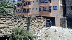 Un edificio residencial de varios pisos con balcones, una pared de piedra en primer plano y un vehículo estacionado.