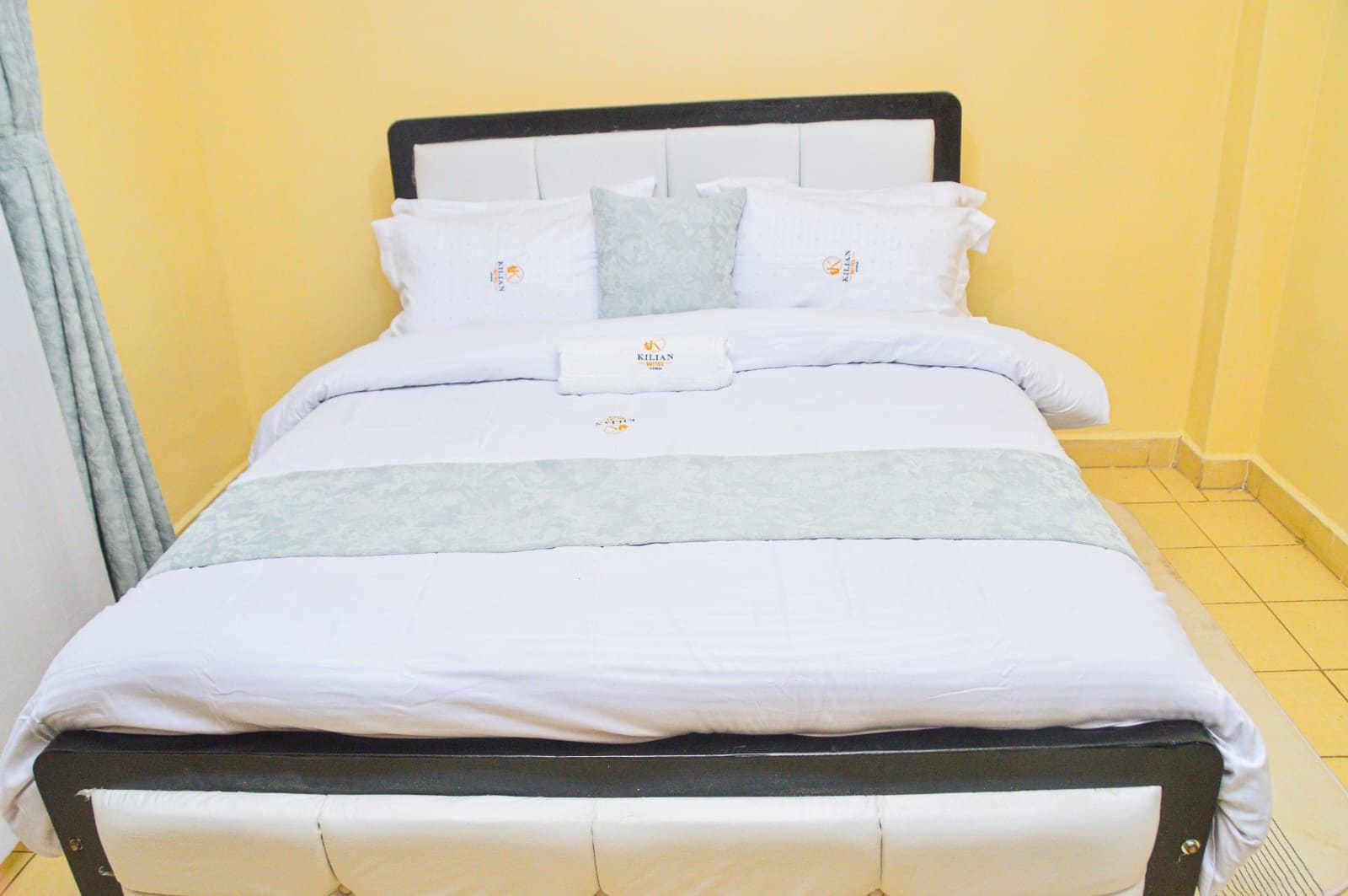 A bed with a black frame, white bedding, and a grey throw blanket.