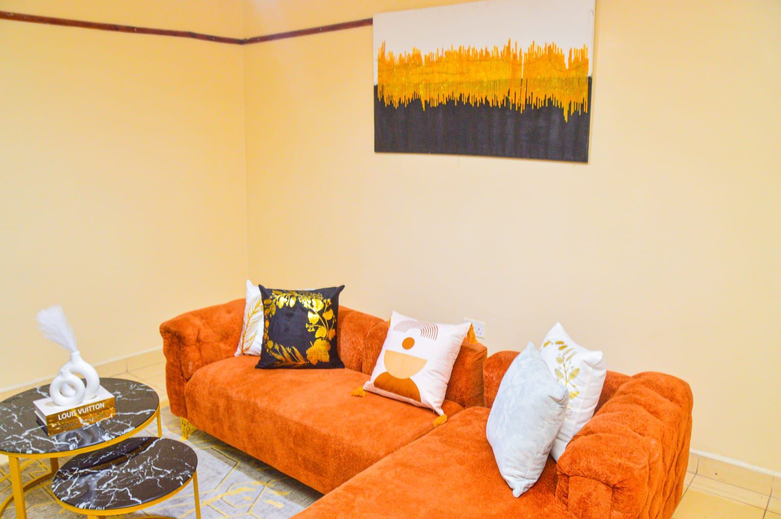 Una habitación con un sofá naranja, una mesita redonda con una caja Louis Vuitton y un cuadro en la pared.