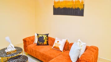 Una habitación con un sofá naranja, una mesita redonda con una caja Louis Vuitton y un cuadro en la pared.