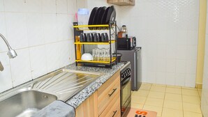 Una cocina con un lavamanos de acero inoxidable, un escurreplatos, un microondas, una estufa a gas y un refrigerador pequeño.