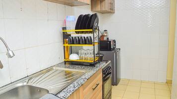 A kitchen with a stainless steel sink, a dish rack, a microwave, a gas stove, and a small refrigerator.