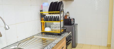 A kitchen with a stainless steel sink, a dish rack, a microwave, a gas stove, and a small refrigerator.