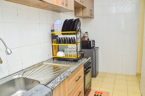 Et køkken med vask i rustfrit stål, opvaskestativ, mikrobølgeovn, gaskogeplade og et lille køleskab.