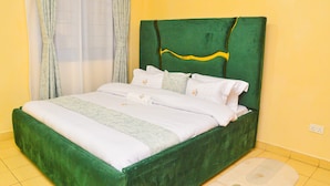 Una cama con cabecera verde, ropa de cama blanca y una alfombra de color claro.