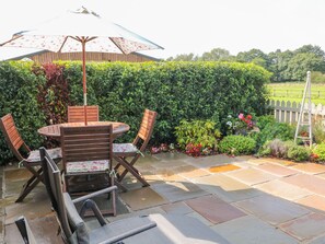 An outdoor patio with a round table and chairs, a wooden fence, and a variety of plants and flowers. - The Byre (Ashbourne)
