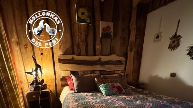 A cozy bedroom with a wooden bed, a nightstand, and a wall-mounted lamp. - Soothing 2-bedroom cottage perfect for a relaxing getaway (Chile)