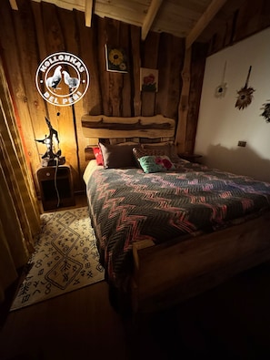 A cozy bedroom with a wooden bed, a nightstand, and a wall-mounted lamp. - Soothing 2-bedroom cottage perfect for a relaxing getaway (Chile)