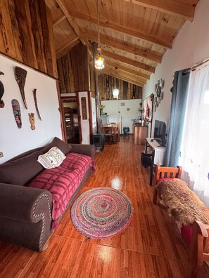 A cozy living room with a wooden ceiling, a sofa, a TV, and a dog.