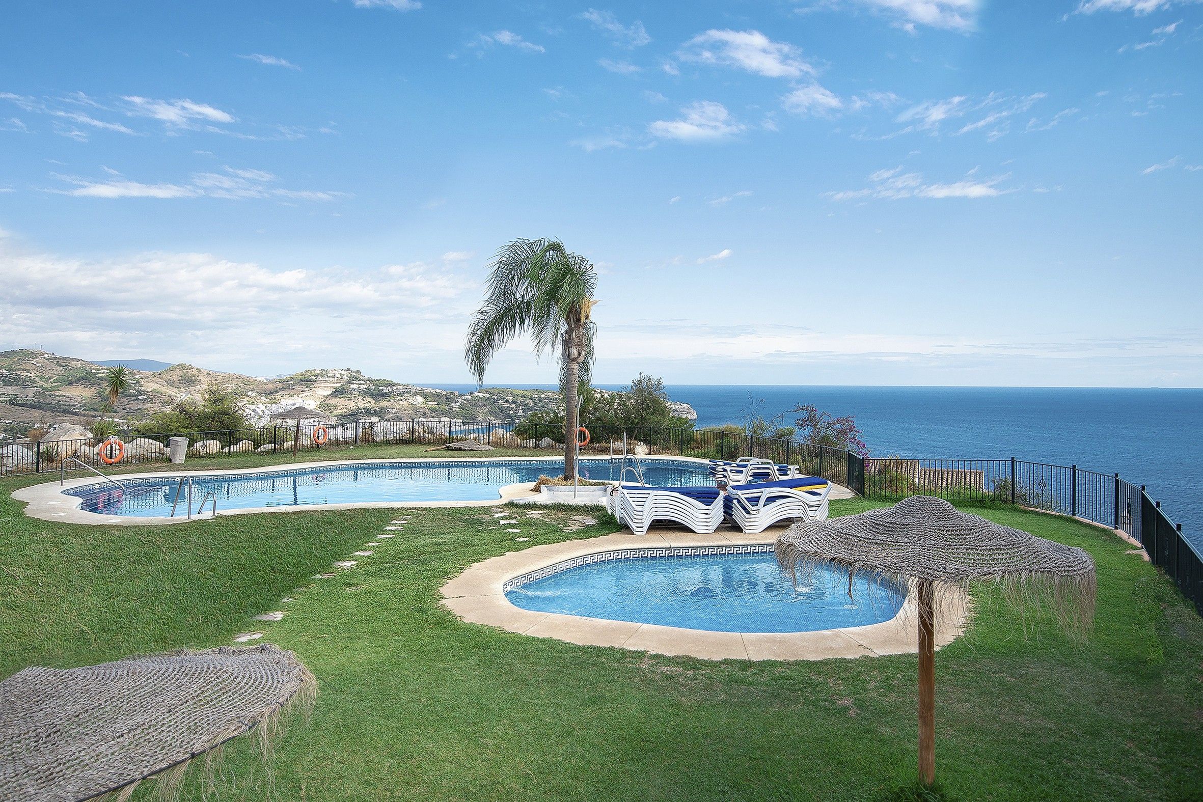 A pool area with multiple swimming pools, lounge chairs, and a view of the sea.