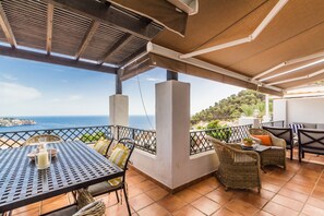 Eine Terrassenanlage im Freien mit Tisch und Stühlen, Meerblick und einem überdachten Bereich mit Geländer.