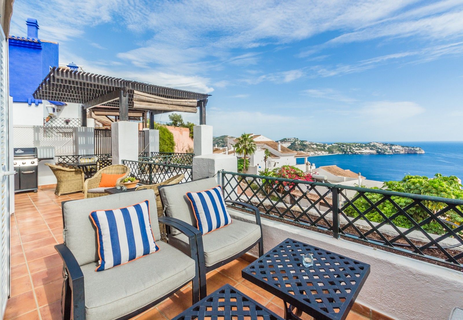 A terrace with outdoor furniture, a grill, and a view of the sea.