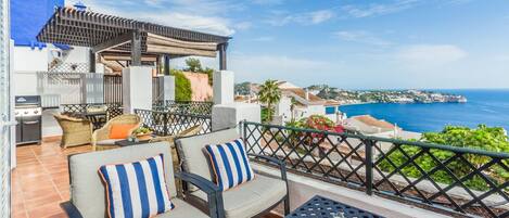 A terrace with outdoor furniture, a grill, and a view of the sea.