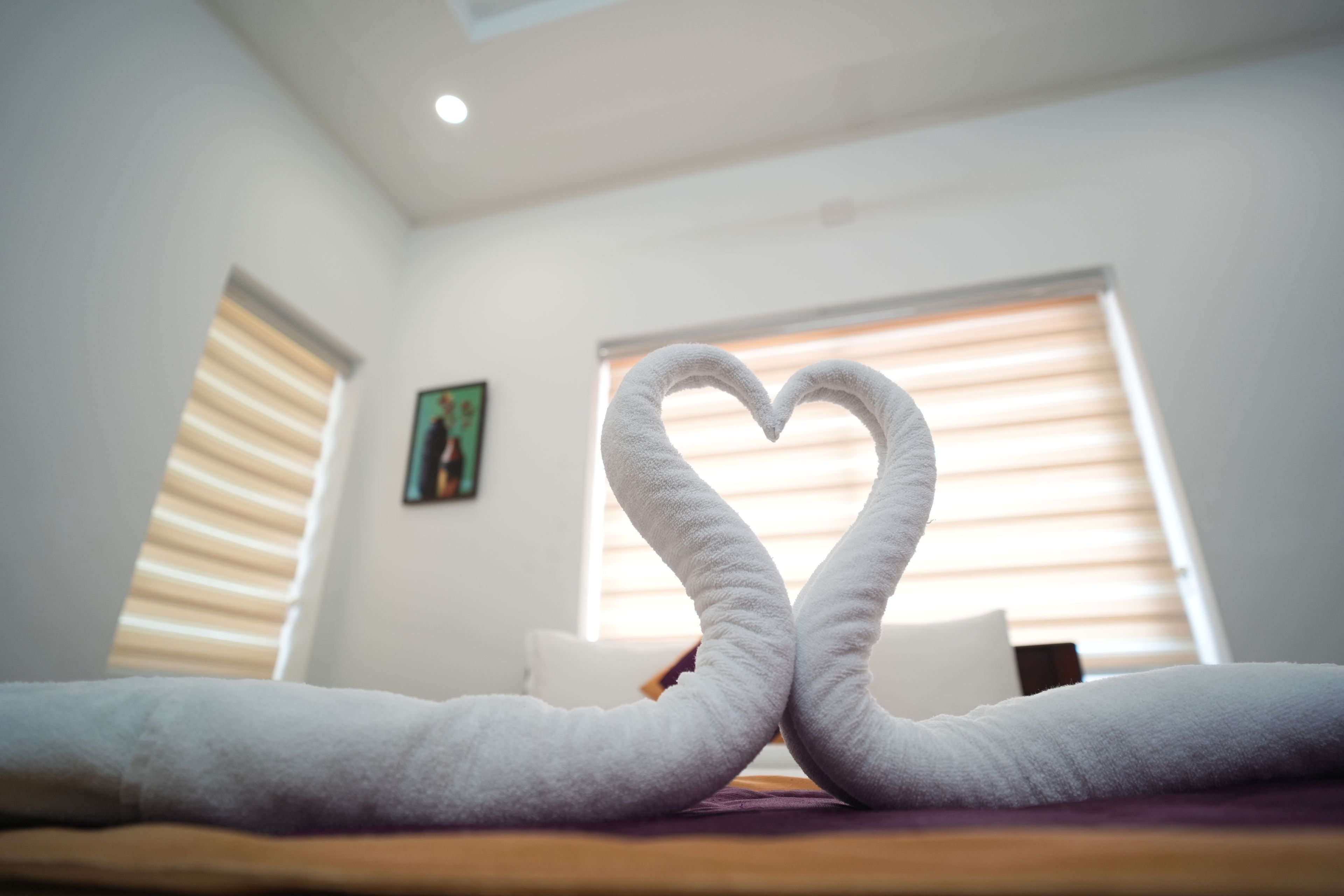 Ein Zimmer mit einem Bett, einer herzförmig drapierten Handtuchgarnitur und einem Bild an der Wand.