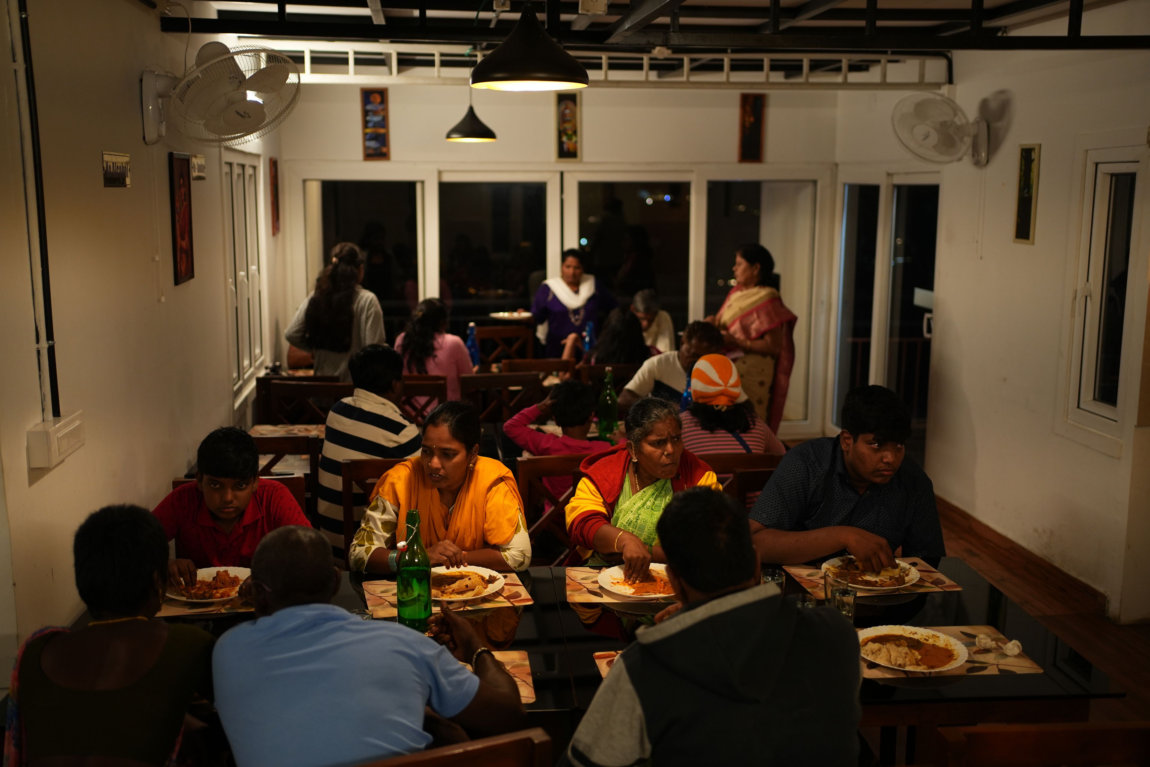 Ein Restaurant mit mehreren Tischen und Stühlen, Gäste beim Essen und einige stehende Personen.