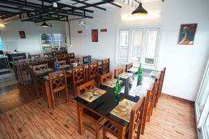 A restaurant with wooden tables and chairs, a kitchen area, and a view of the outdoors.
