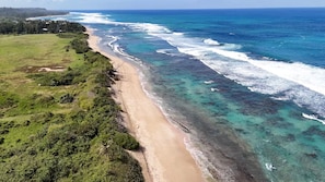 Eine Küstenlandschaft mit einem Sandstrand und klarem türkisblauem Wasser.