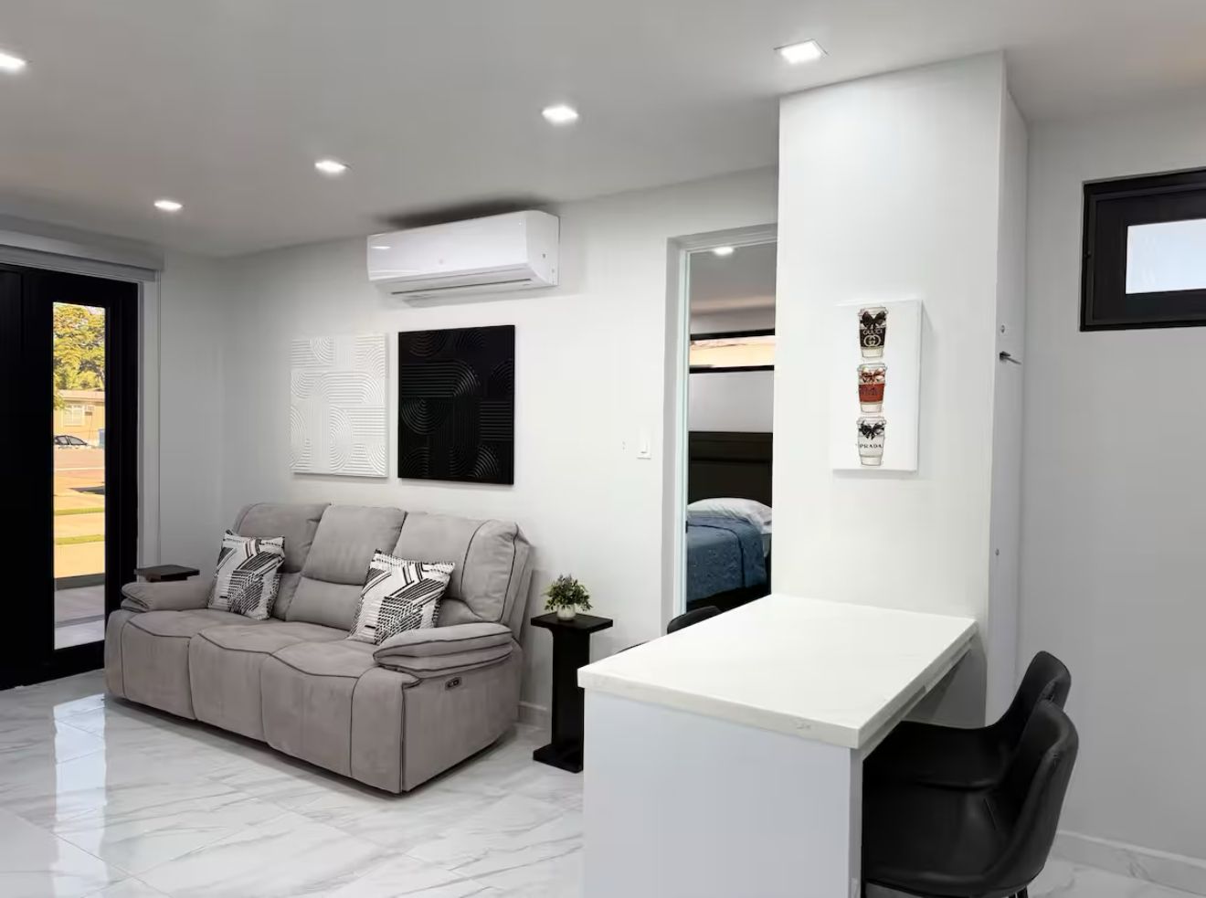 Ein modernes Wohnzimmer mit einer Couch, einem weißen Schreibtisch und einem Bett im Hintergrund.