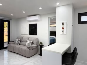 Un salon moderne avec un canapé, un bureau blanc et un lit en arrière-plan.