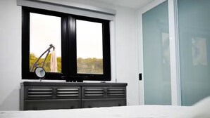 Quarto moderno com cama, penteadeira, janela com vista e porta deslizante.