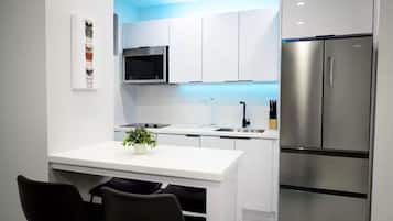 Una cocina moderna con armarios blancos, un refrigerador de acero inoxidable, un microondas y una pequeña isla con una planta.