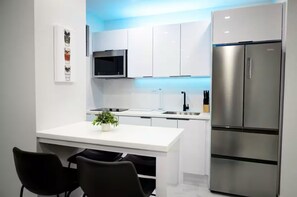 Une cuisine moderne avec des meubles blancs, un réfrigérateur en acier inoxydable, un four à micro-ondes et un petit îlot central agrémenté d’une plante.