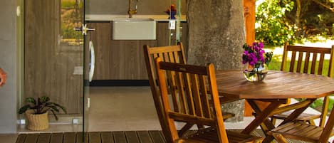 A wooden deck with a table and chairs, a stone pillar, and a view of a kitchen and garden.
