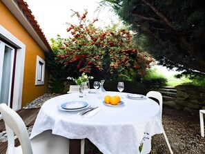 An outdoor dining area with a table set for two, surrounded by a stone wall and a bush with red berries. - Country House 'D’Olívia Lovely Homes -Casa Olívia' with Shared Garden, Wi-Fi and Air Conditioning (Cela)
