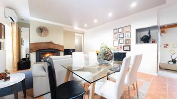 A modern dining area with a glass table, white chairs, and a fireplace.