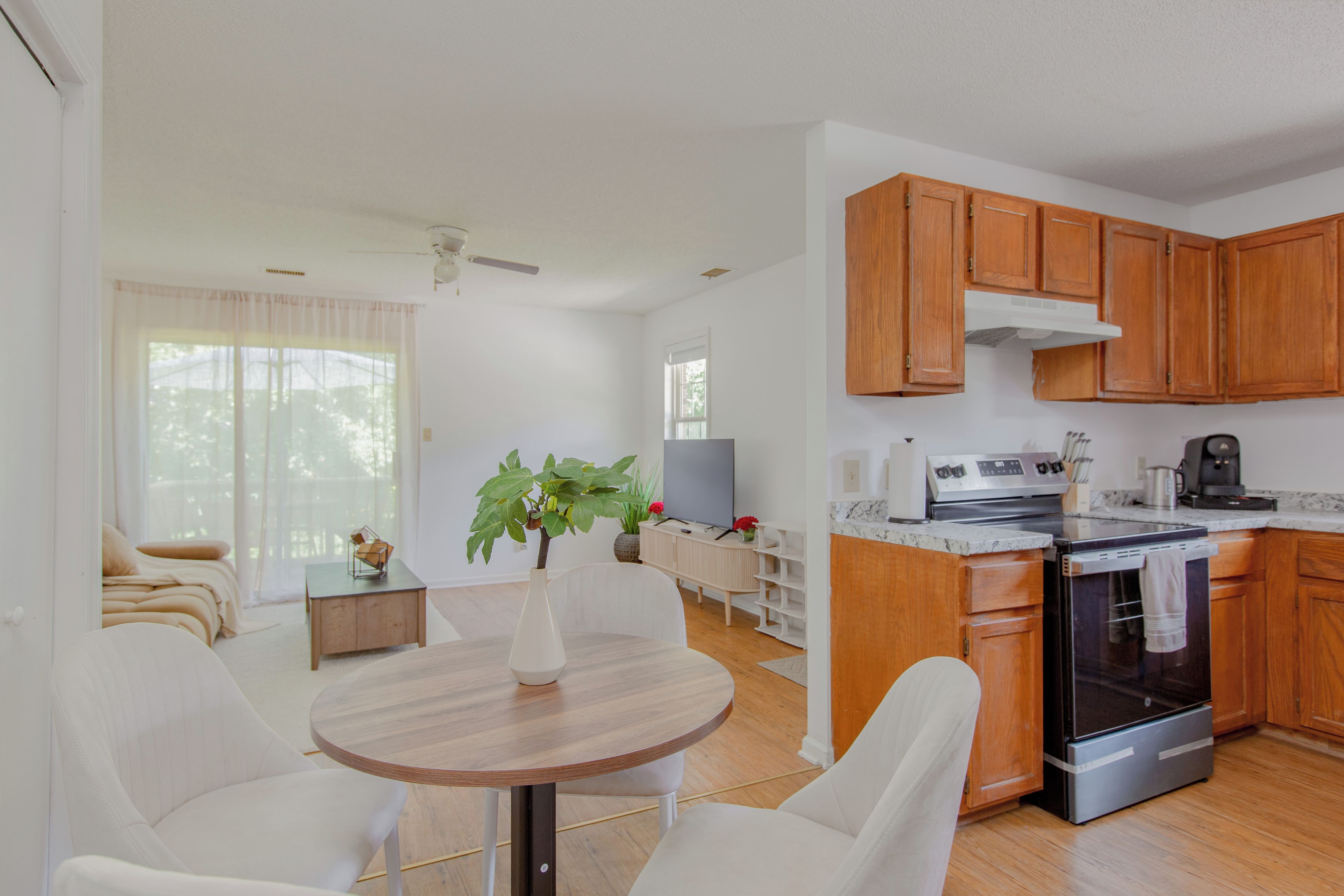 A modern kitchen with wooden cabinets, a built-in oven, and a dining area with a round table and white chairs.