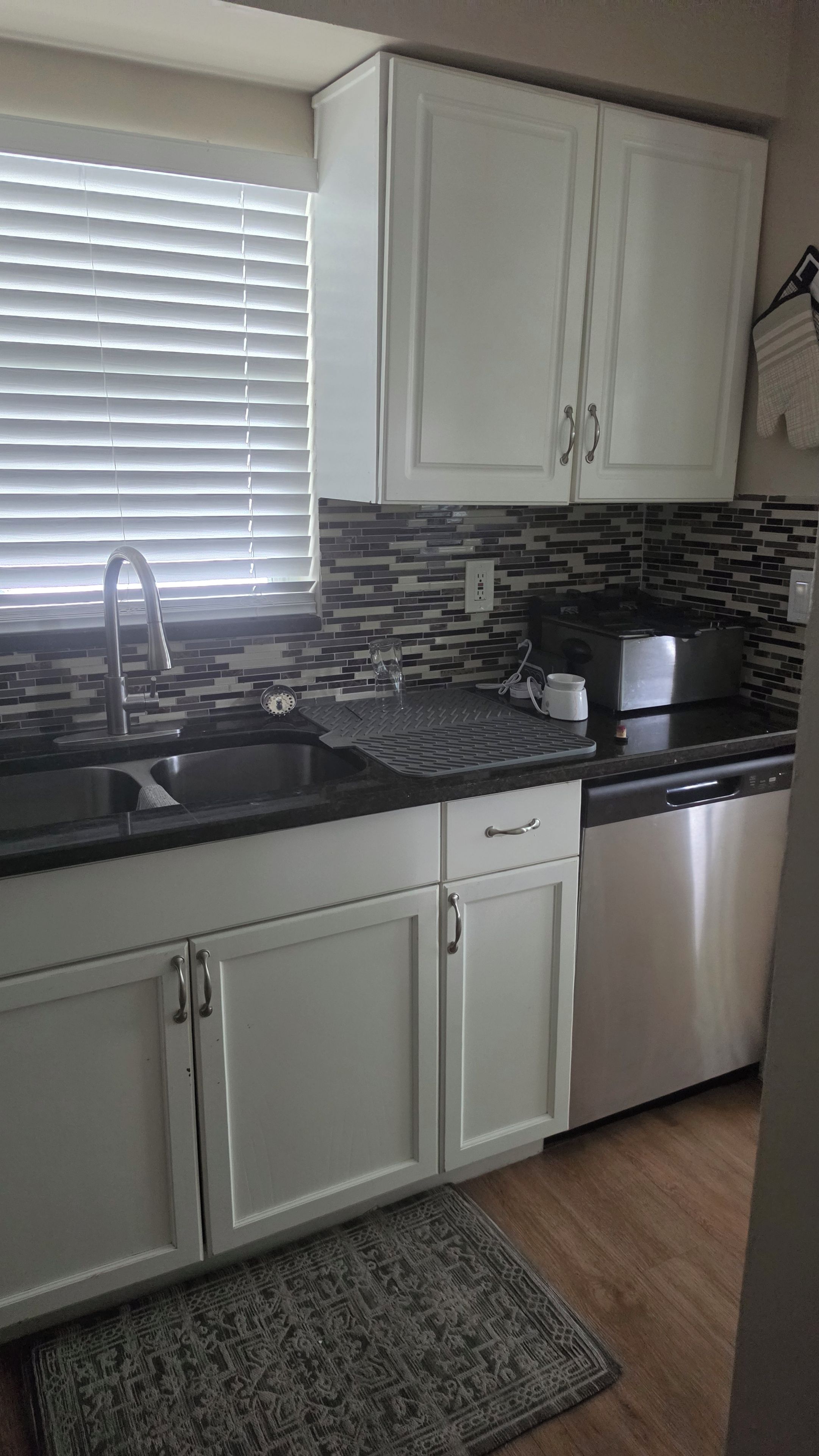 A kitchen with white cabinets, a stainless steel sink, a black countertop, and a patterned backsplash.
