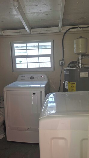 A laundry room with a front-loading washing machine, a dryer, and a water heater. -  Spacious Orlando Getaway 3 Bd 1bt- 6 Beds with huge  Backyard for entertainment (Orlando)