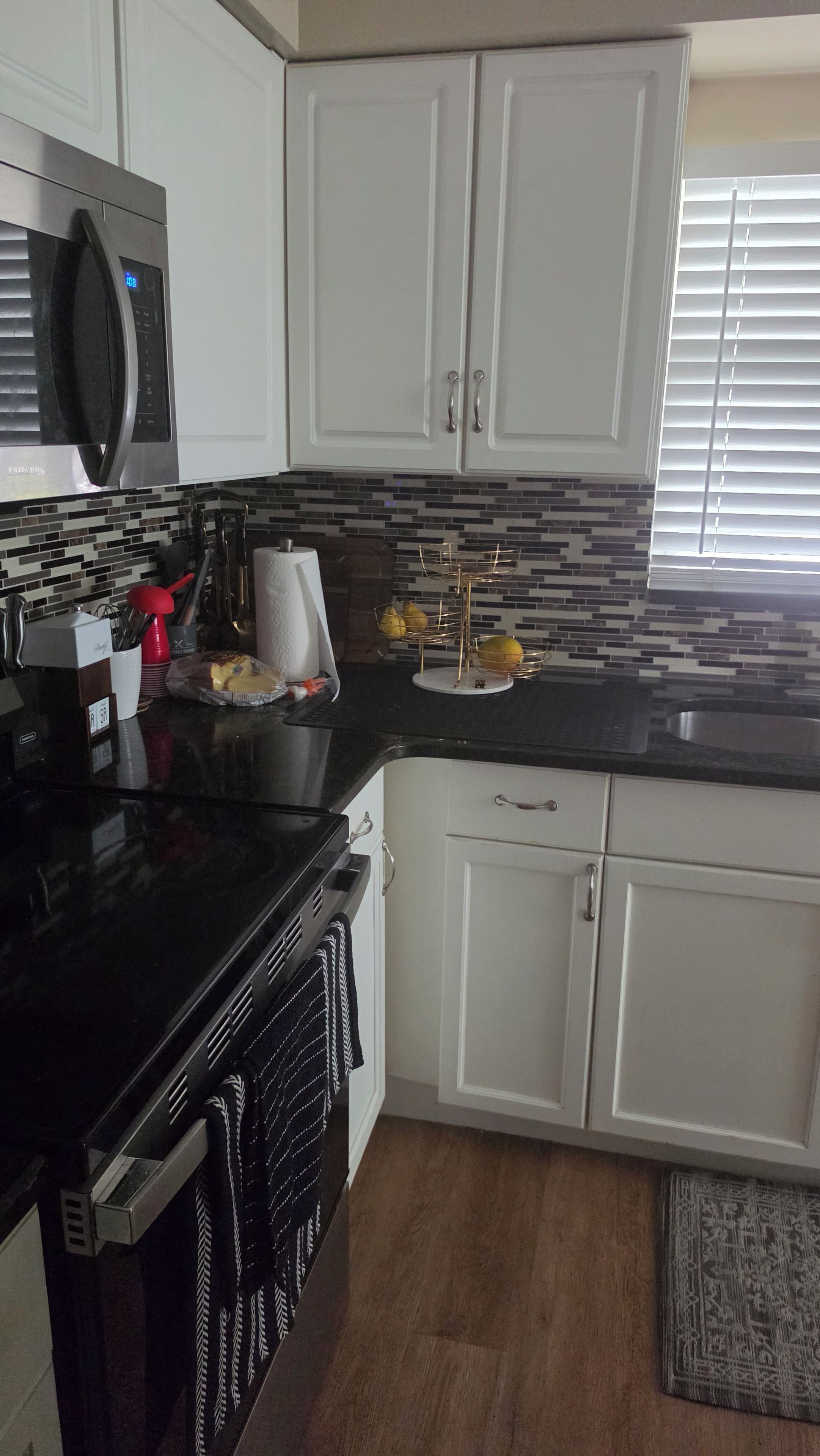 A kitchen with white cabinets, a black countertop, a microwave, and a dish rack with lemons.