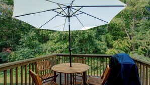 Une terrasse en bois avec une table ronde et quatre chaises, un parasol et un barbecue.