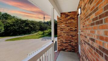 A covered porch with a brick wall and a view of a road and greenery.