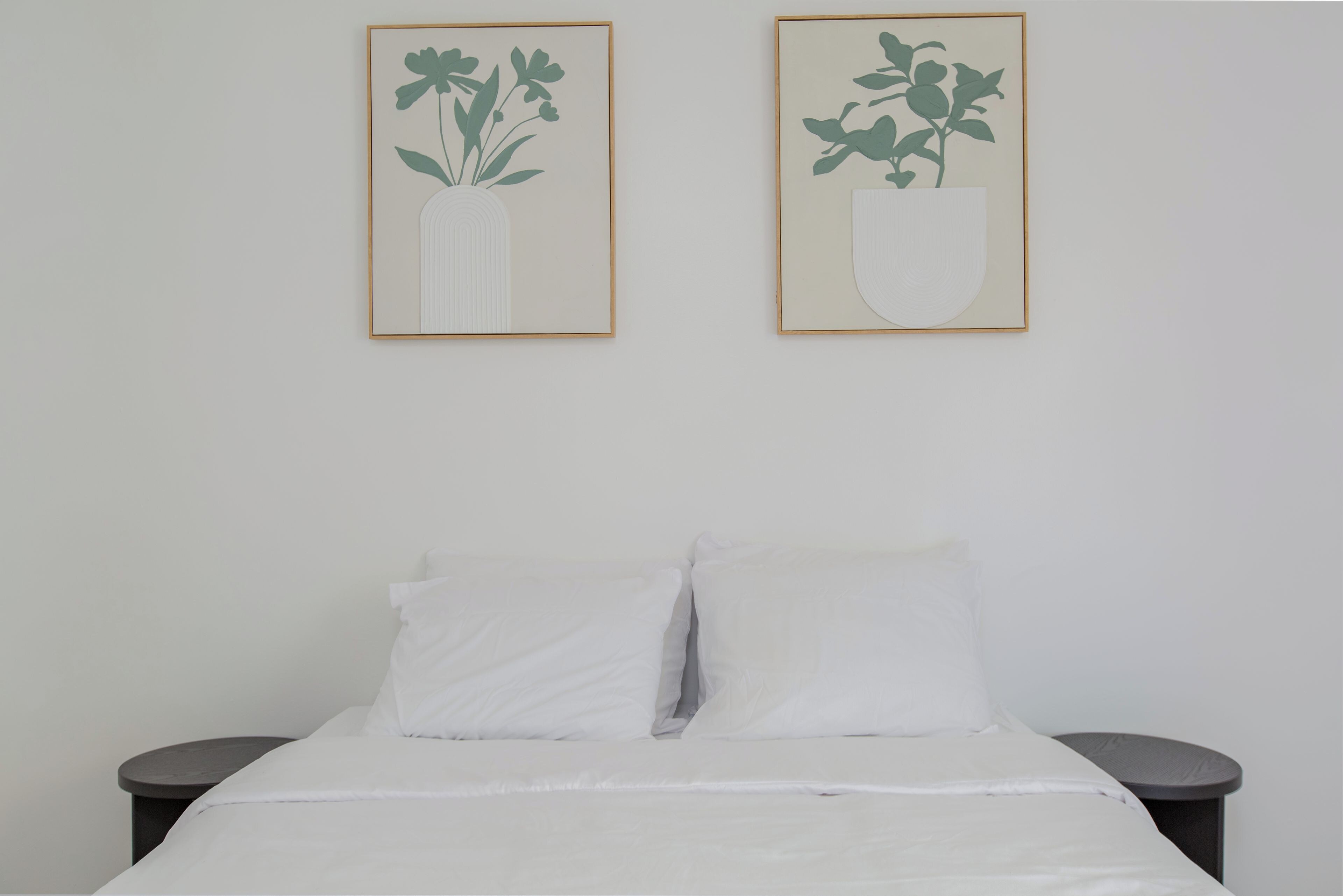 Cama com roupa de cama branca e duas mesas de cabeceira redondas de cada lado.