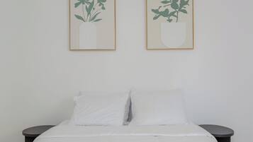 Cama com roupa de cama branca e duas mesas de cabeceira redondas de cada lado.
