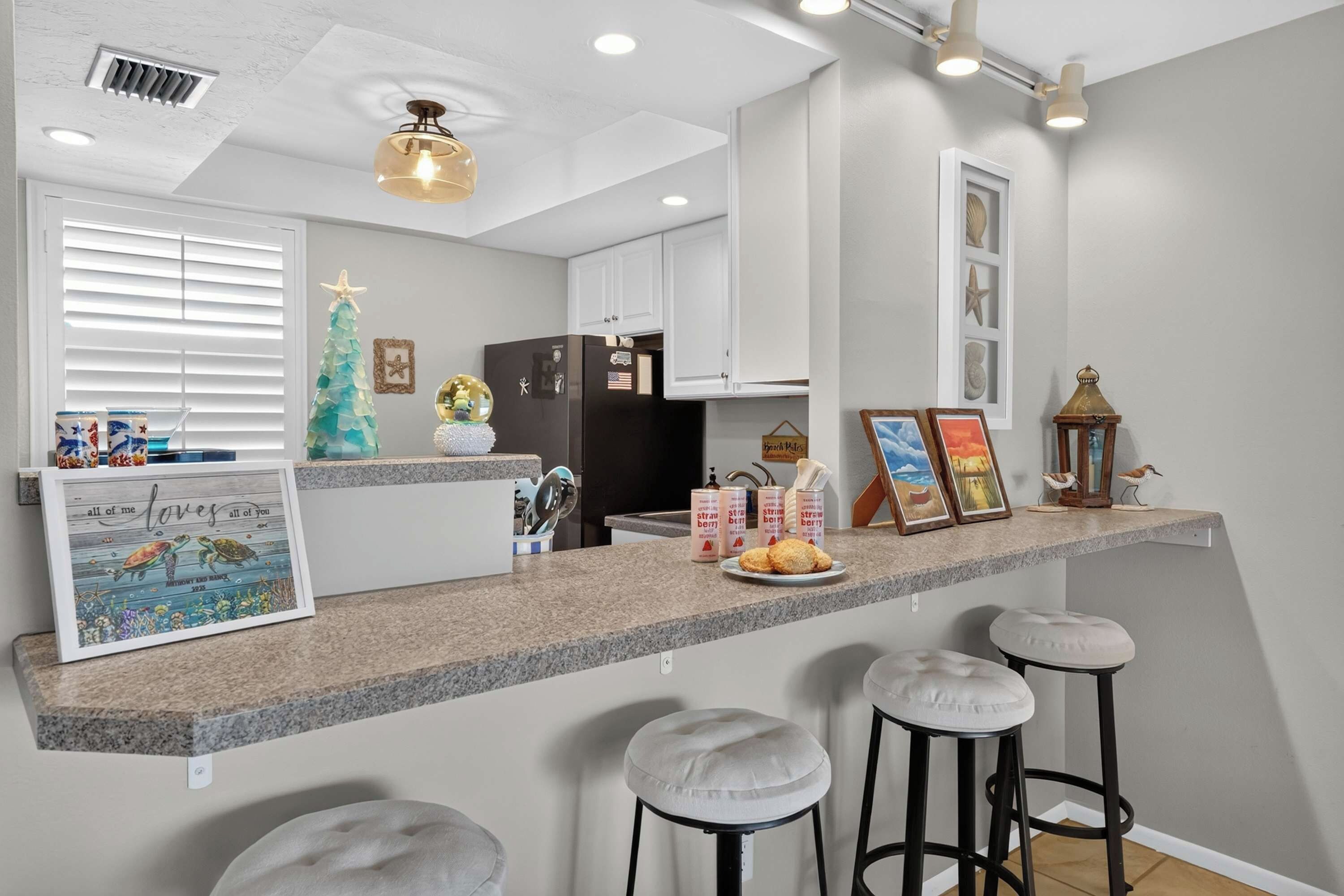 A kitchen with a granite countertop, a refrigerator, and a dining area with stools.