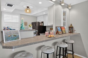 A kitchen with a granite countertop, a refrigerator, and a dining area with stools. - Bay View at Sutton Place | Longboat Key | Beach Access | 30-Day Min (Longboat Key)
