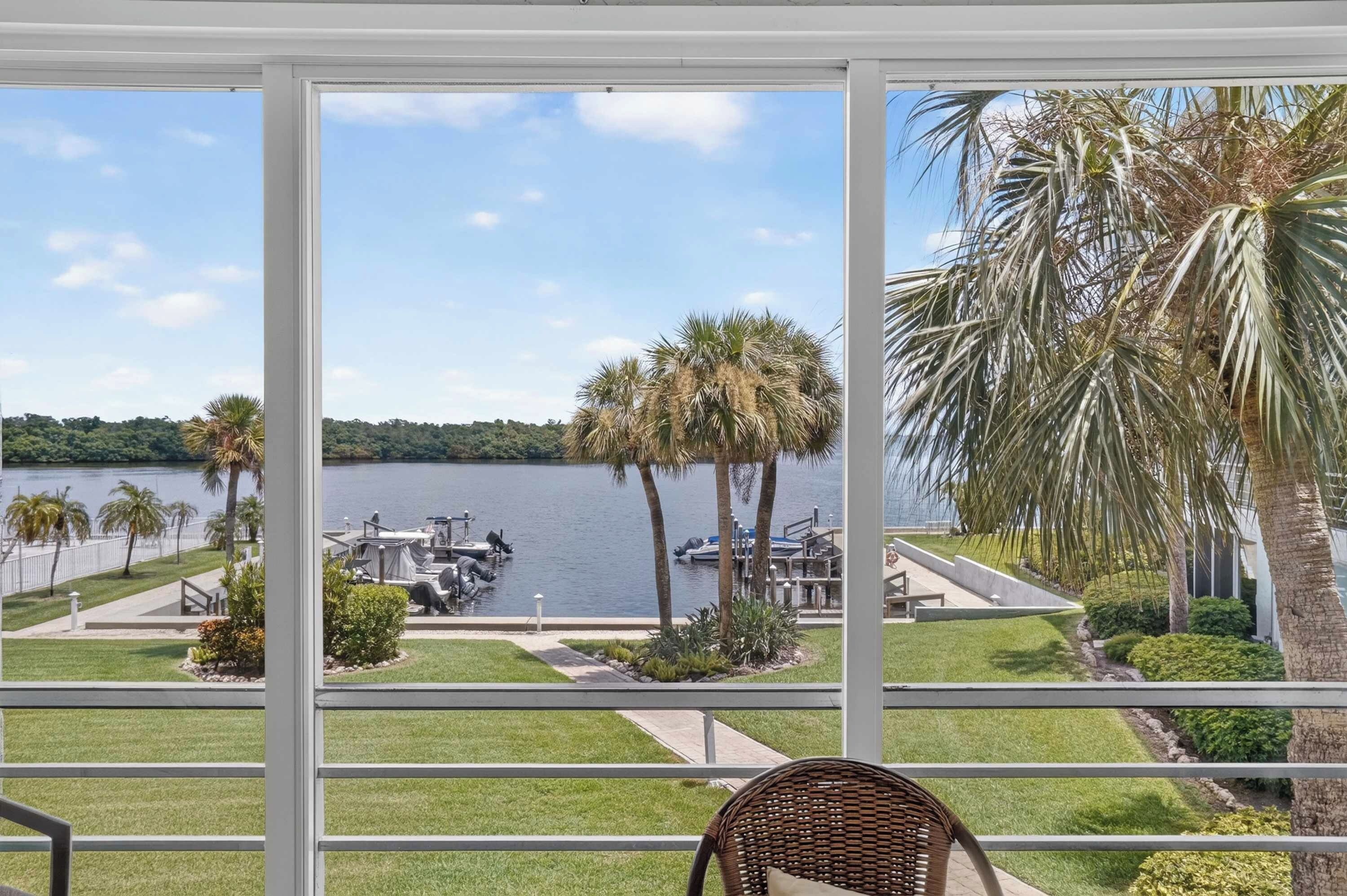 A view from a balcony overlooking a lake with boats, palm trees, and a dock area.