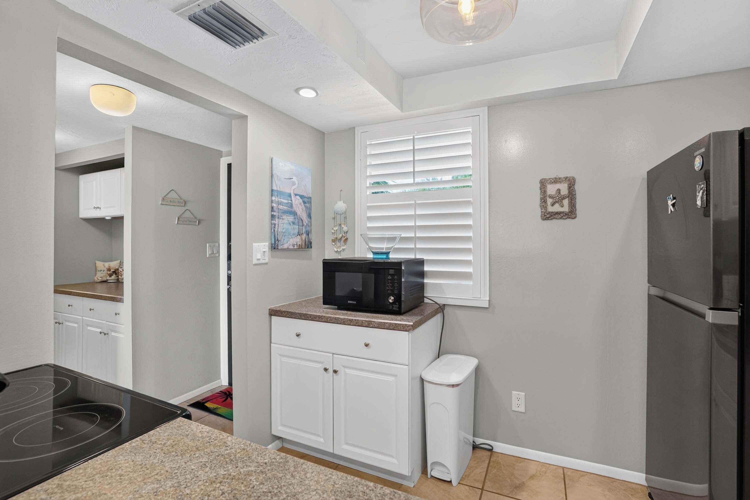 A modern kitchen with white cabinetry, a black microwave, and a stainless steel refrigerator.