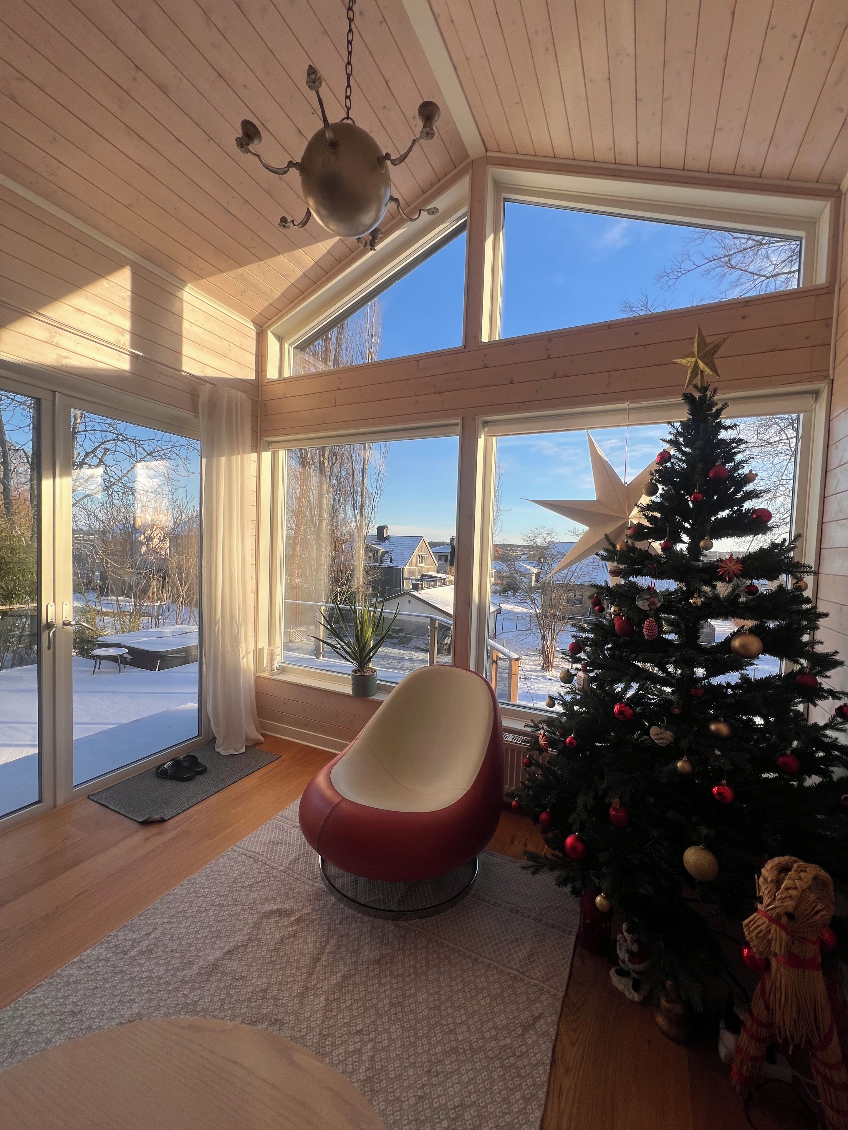 Et værelse med et stort vindue, et juletræ og en rød stol.