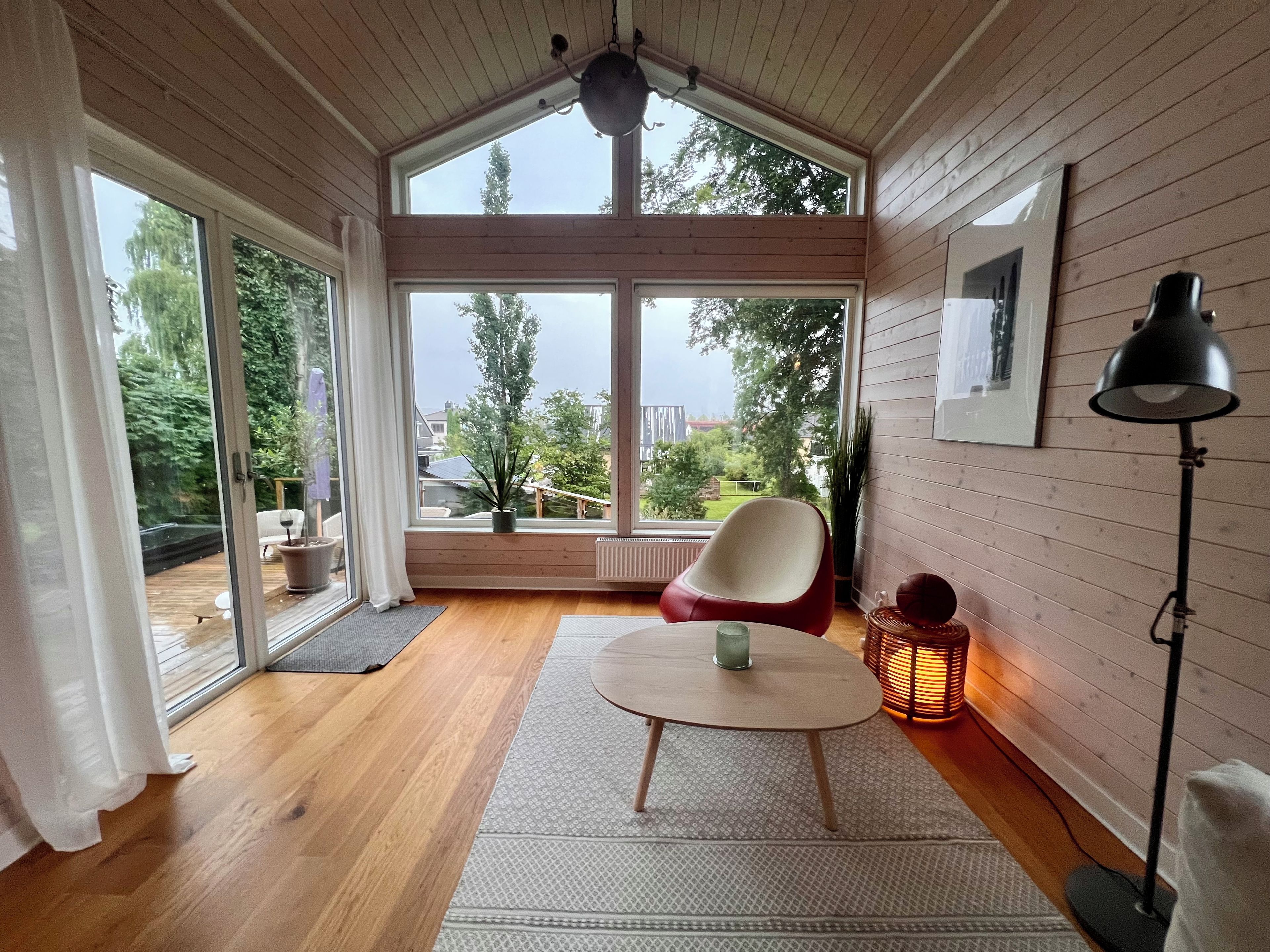 Una habitación con un ventanal grande, una mesa redonda, una silla, una lámpara de pie y un radiador.