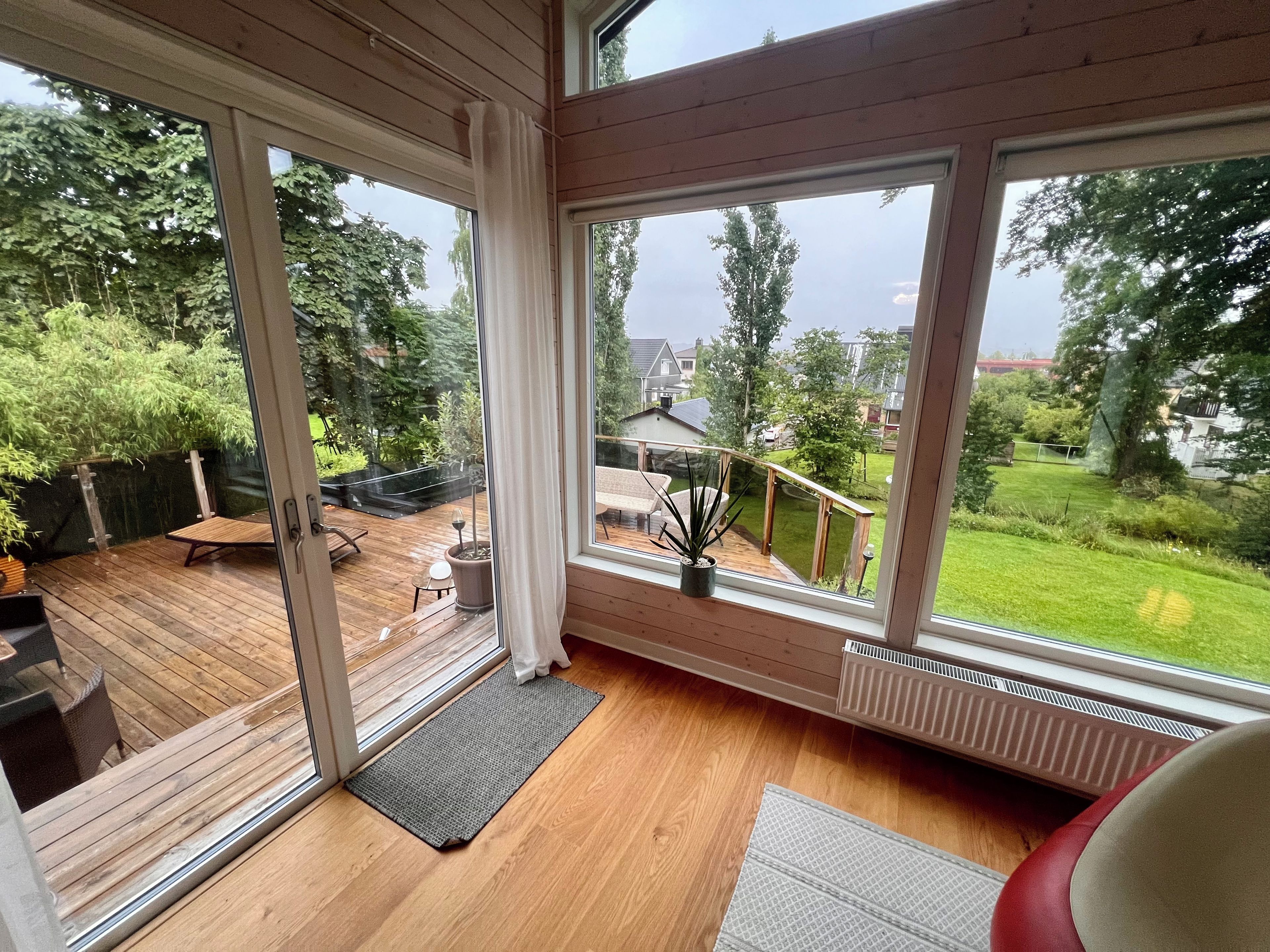 A room with large windows, a wooden deck, and a view of a garden.