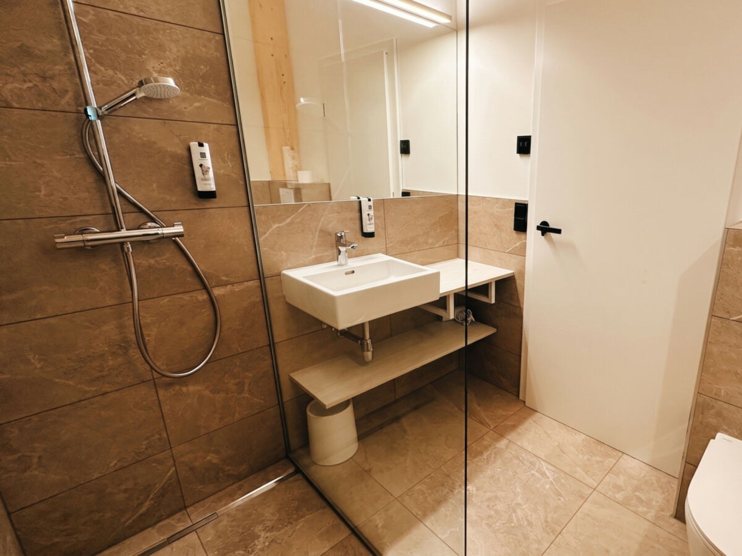 Moderni kylpyhuone, jossa on lasinen suihkuseinä, valkoinen pesuallas ja wc-istuin.