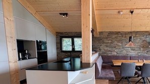 Una cocina moderna con una isla central, vigas de madera en el techo y una pared de piedra.