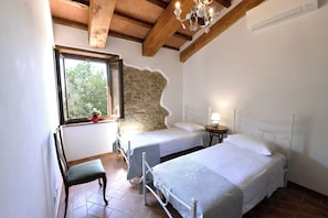 Quarto com duas camas, uma cadeira, uma janela e uma parede de pedra.