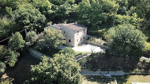 A stone building surrounded by dense greenery, with a paved area in front. - Charming Italian Farmhouse with Sunset views, Ensuites & Private Infinity Pool (Umbria)