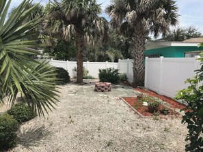 Un jardín con palmeras, un hogar de fuego de ladrillo y una valla blanca.